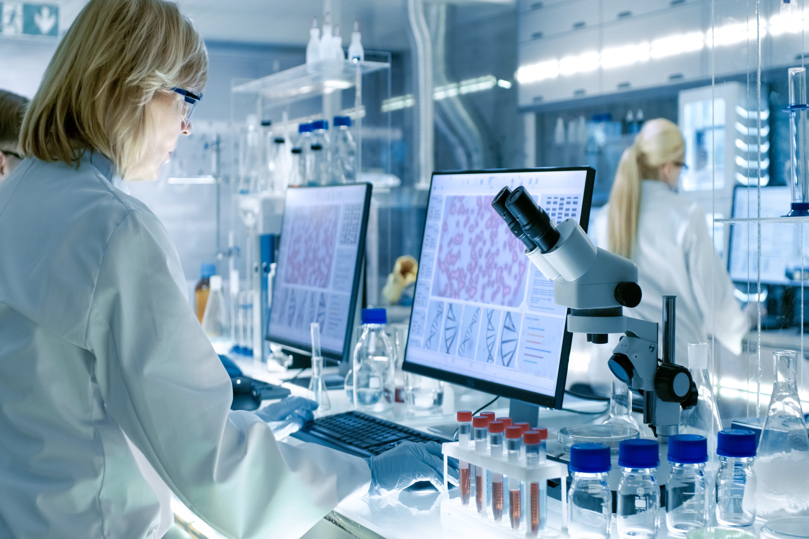Senior Female Scientist Works with High Tech Equipment in a Modern Laboratory. Her Colleagues are Working Beside Her. Senior Female Scientist Works with High Tech Equipment in a Modern Laboratory. Her Colleagues are Working Beside Her.